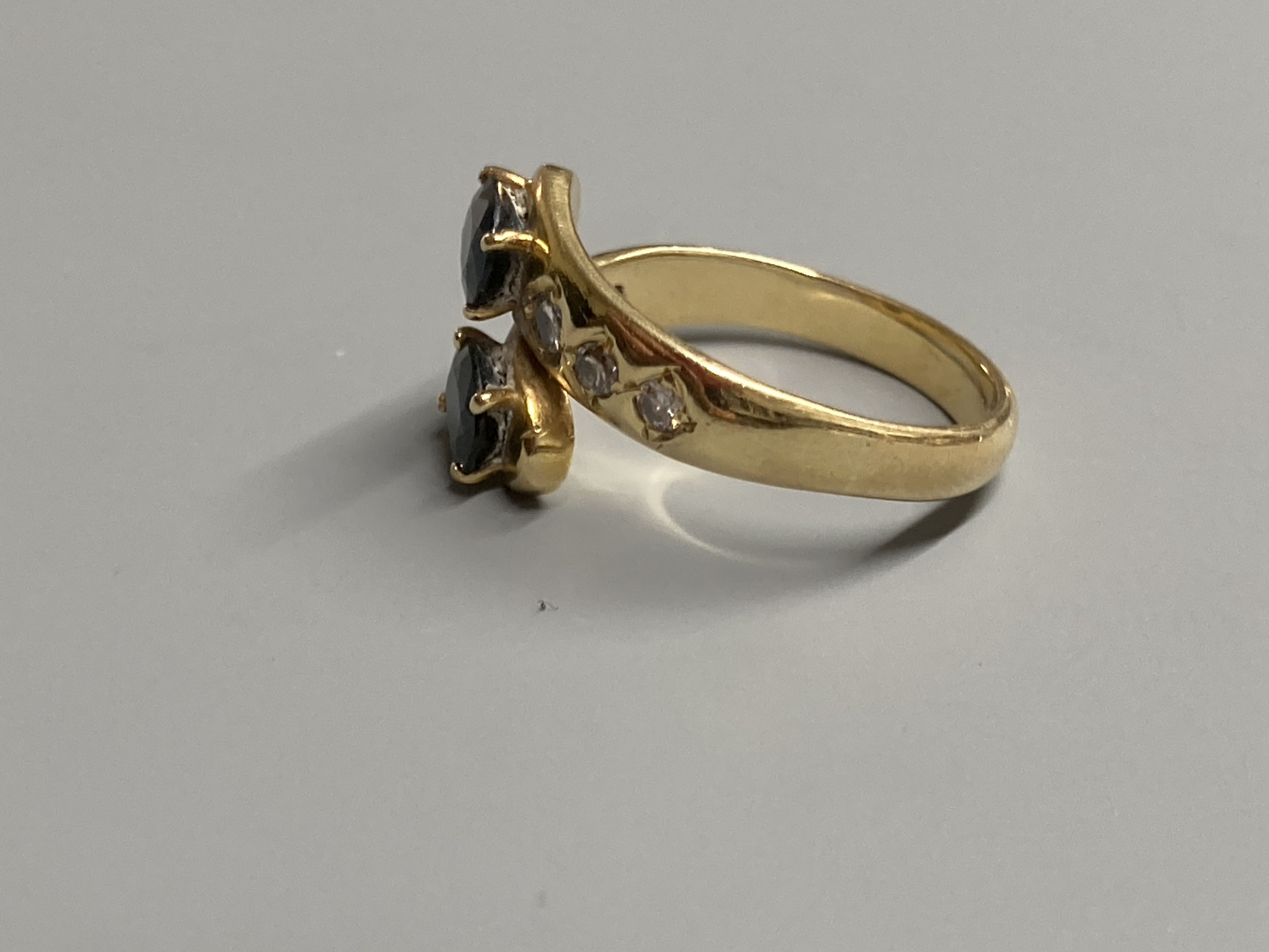 A modern 18ct and two stone sapphire crossover ring, with diamond set shoulders, size P, gross 5.4 grams.